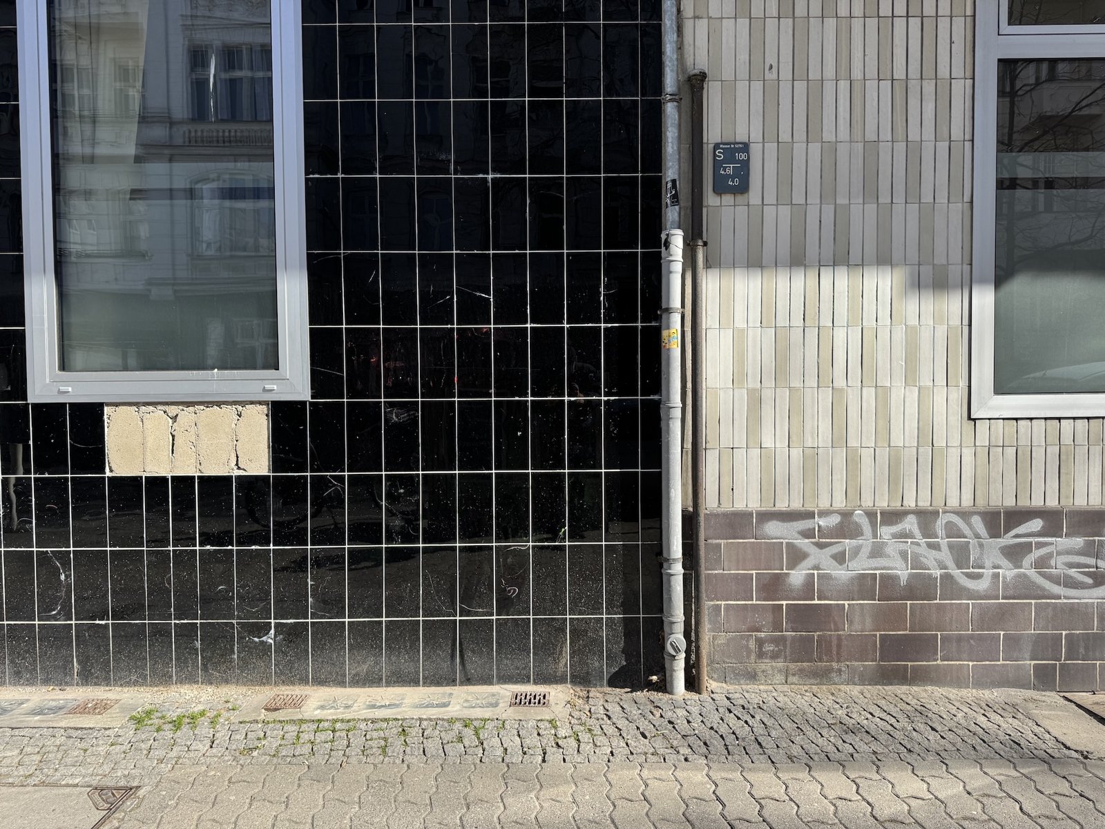 Black glossy tile facade against cream brick in raking light, Berlin