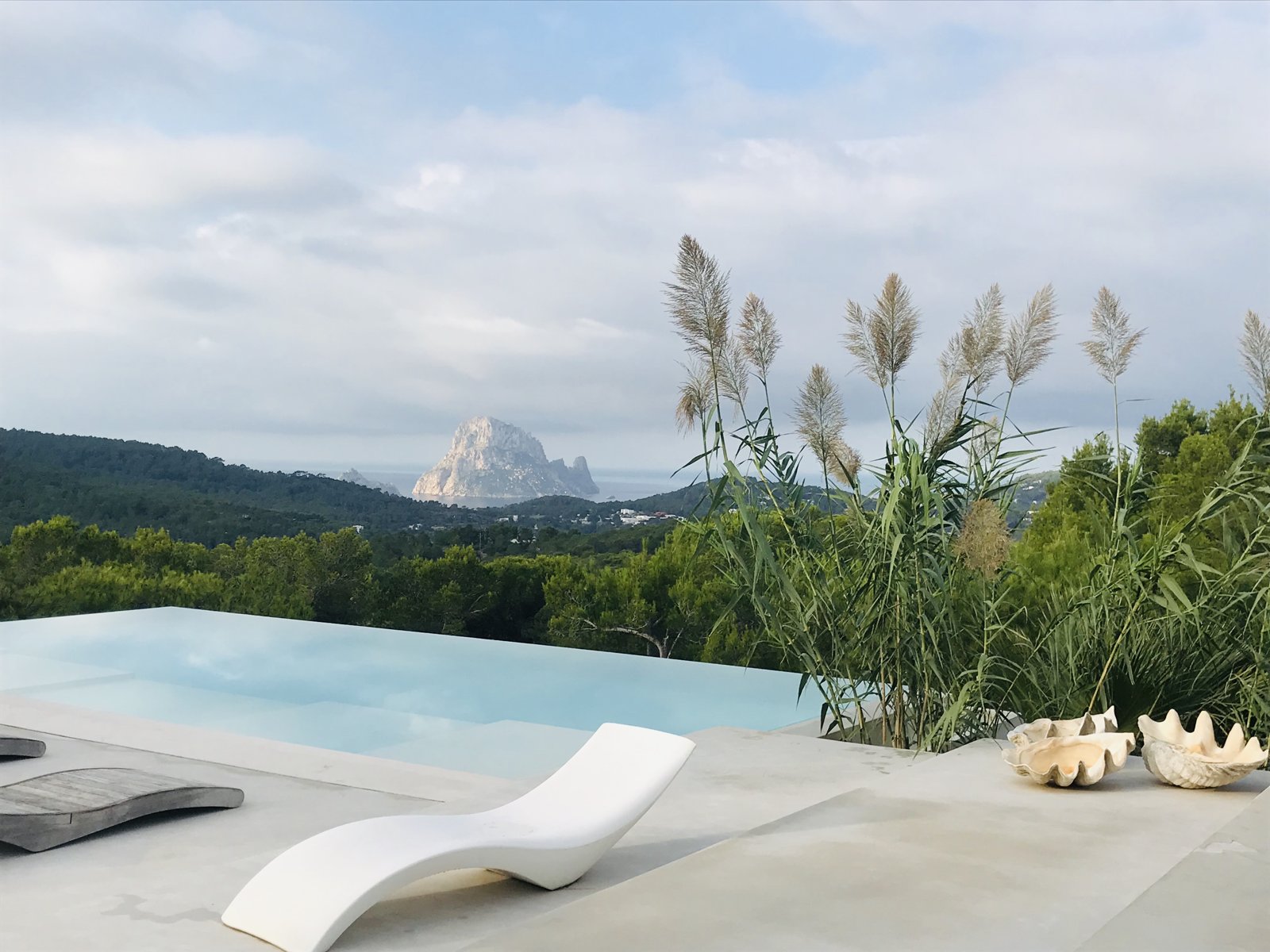 Infinity pool with a white lounger framing Es Vedrà across pine hills, Ibiza